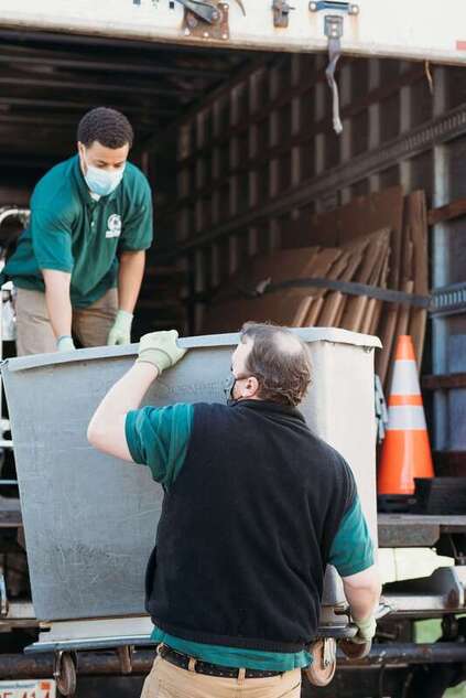 Two workers moving a bin into a truck